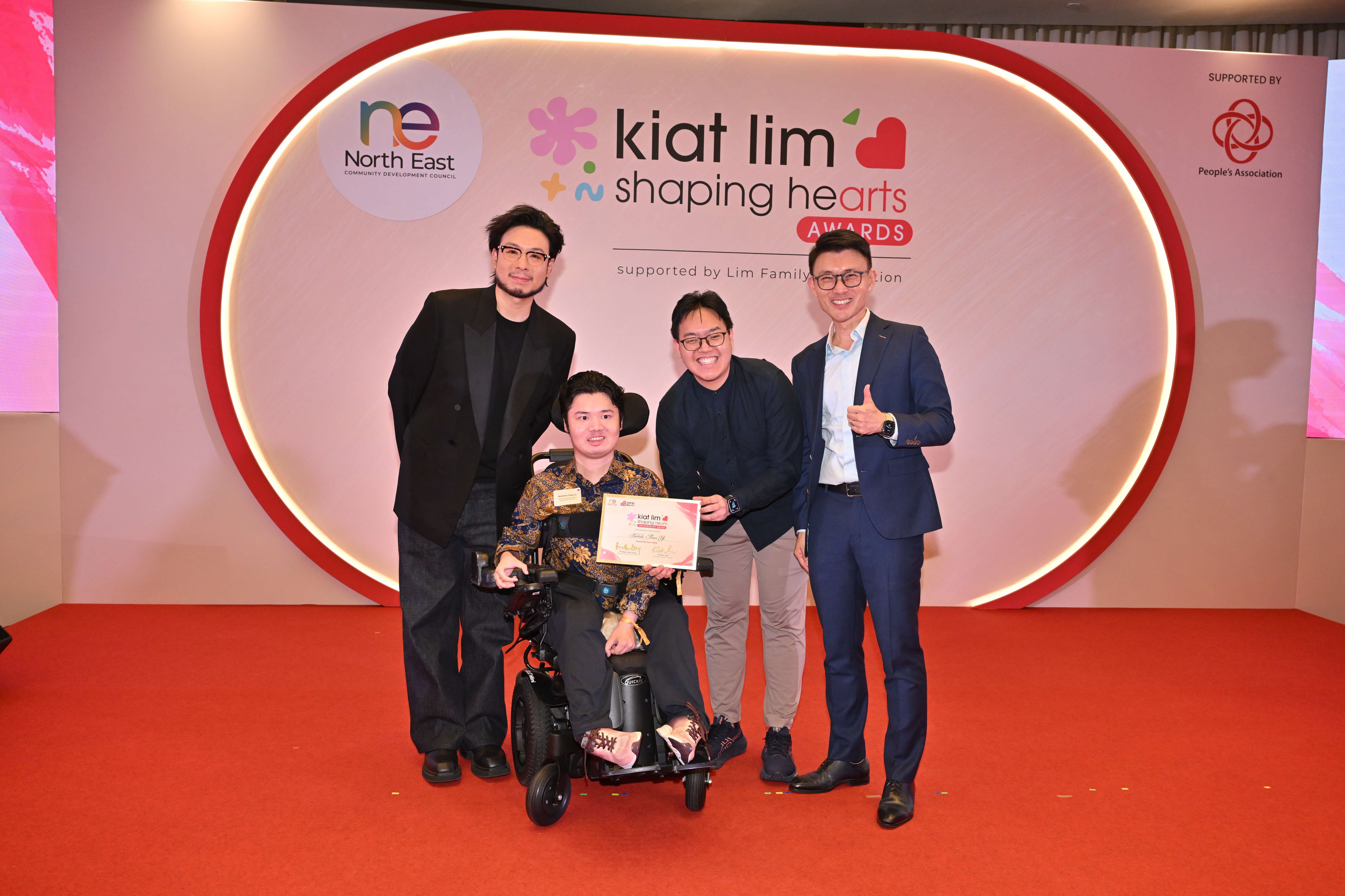 Award recipient standing on stage with the presenter, holding their certificate and posing for a group photo during the award ceremony, with a backdrop reading ‘Kiat Lim-Shaping Hearts Awards'.